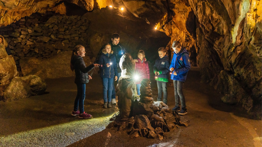 Kundige Führer erklären den Kindern im Schein der Taschenlampen, wie die Tropfsteine wachsen. Foto: DJD/Stadt Oberharz am Brocken/Jan Reichel