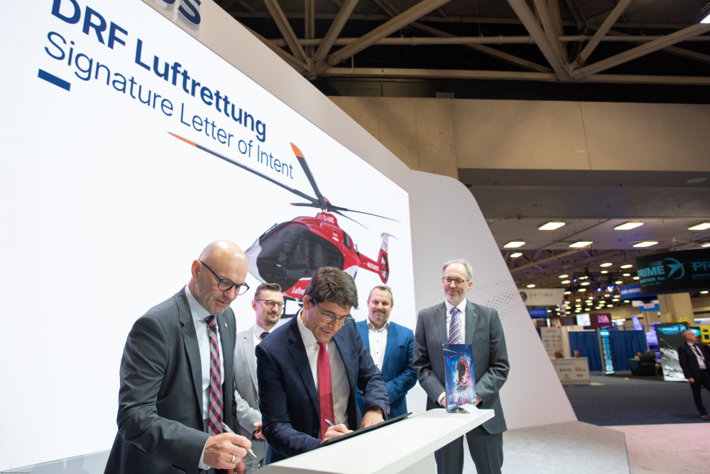 Unterschrift unter den Letter of Intent auf der Verticon in Dallas/Texas. Quelle: Airbus Helicopters/Dianne Baker BondZwei Männer in Anzug und Krawatte halten ein Bild eines rot-weißen Hubschraubers vor blauem Hintergrund.Dr. Krystian Pracz, CEO DRF Luftrettung, und Bruno Even, CEO Airbus Helicopters, bei 