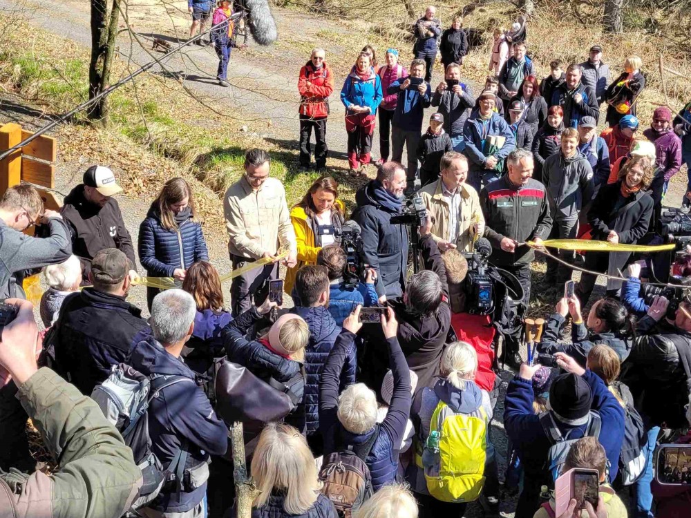 Foto Hp. Mayr Mit großem öffentlichen Interesse wurde das Band zur Eröffnung des neuen grenzübergreifenden Wanderweges im Tal Suchá Bělá (Dürre Biele) im Nationalpark Böhmische Schweiz durchschnitten.  Das Band haben durchschnitten (von rechts):  Uwe Borrmeister, Leiter der Nationalpark und Forstverwaltung Sächsische Schweiz von Sachsenforst (grüne Jacke),  Staatssekretär für Umwelt und Landwirtschaft Ulrich Menke, der Umweltminister der Tschechischen Republik Igor Červený, Bürgermeisterin von Hřensko Kateřina Horáková, Leiter der Nationalparkverwaltung Böhmische Schweiz Petr Kříž, Generalkonsulin Ph.D. Ivona Valhová,  Leitender Vertreter des Landratsamtes Usti JUDr. Lukas Borovička