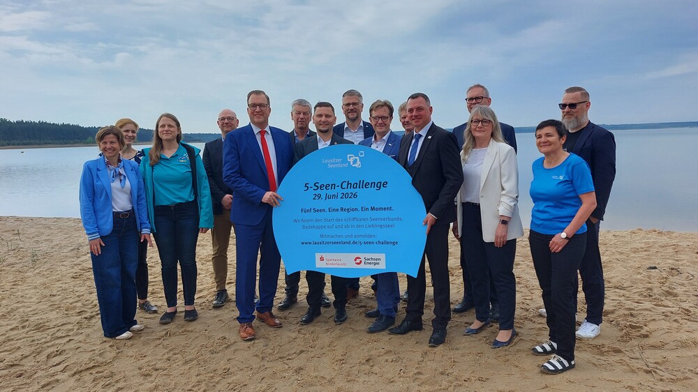 Landräte, Bürgermeister, Zweckverbände, Tourismusverband und Sponsoren werben am Badestrand des Partwitzer Sees für die 5‑Seen‑Challenge am 29. Juni 2026. Mit einem symbolischen Werbeschild in Form einer Badekappe machen sie auf die Aktion zur Eröffnung des schiffbaren Seenverbundes aufmerksam. Foto: Tourismusverband Lausitzer Seenland, Katja Wersch
